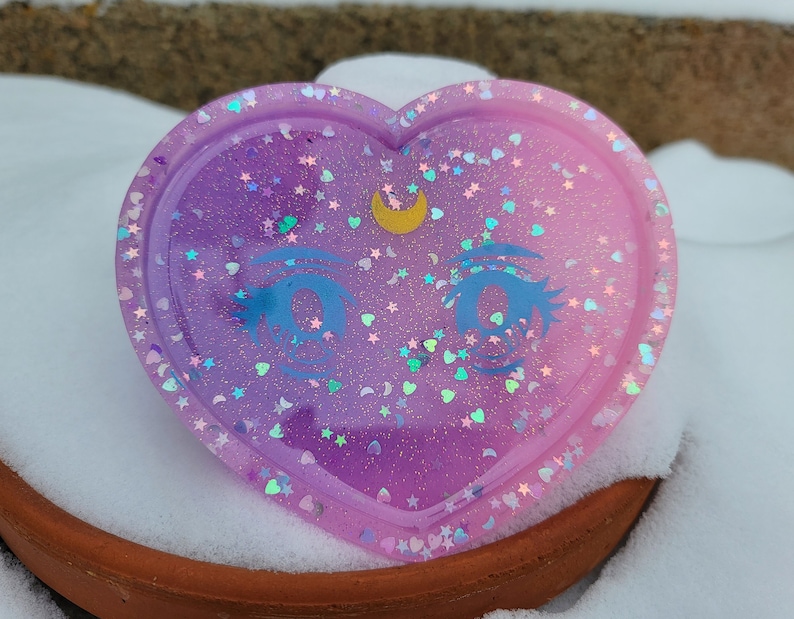 May include: A heart-shaped resin tray with a gradient of pink and purple glitter. The tray features a crescent moon and a pair of anime eyes.