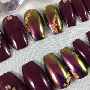 Puede incluir: Conjunto de diez u&ntilde;as postizas en forma de ata&uacute;d. Cinco u&ntilde;as son de color burdeos oscuro, y cinco u&ntilde;as son iridiscentes con destellos dorados.