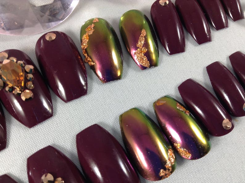 Puede incluir: Conjunto de diez u&ntilde;as postizas en forma de ata&uacute;d. Cinco u&ntilde;as son de color burdeos oscuro, y cinco u&ntilde;as son iridiscentes con destellos dorados.