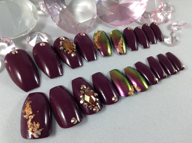 Puede incluir: Conjunto de u&ntilde;as postizas de ata&uacute;d color burdeos con detalles dorados y pedrer&iacute;a.