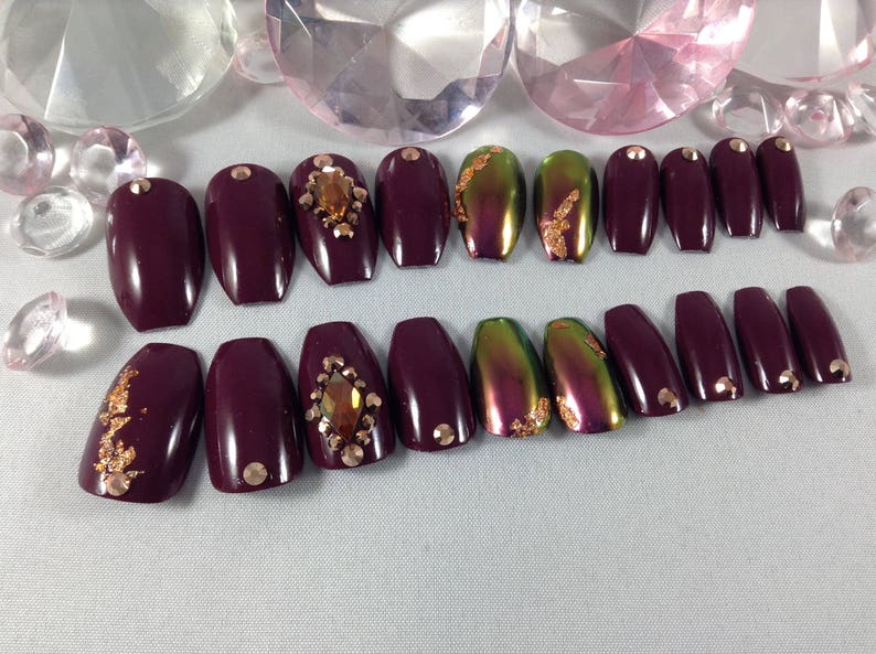 Puede incluir: Conjunto de 10 u&ntilde;as postizas de ata&uacute;d color burdeos con detalles dorados y pedrer&iacute;a.