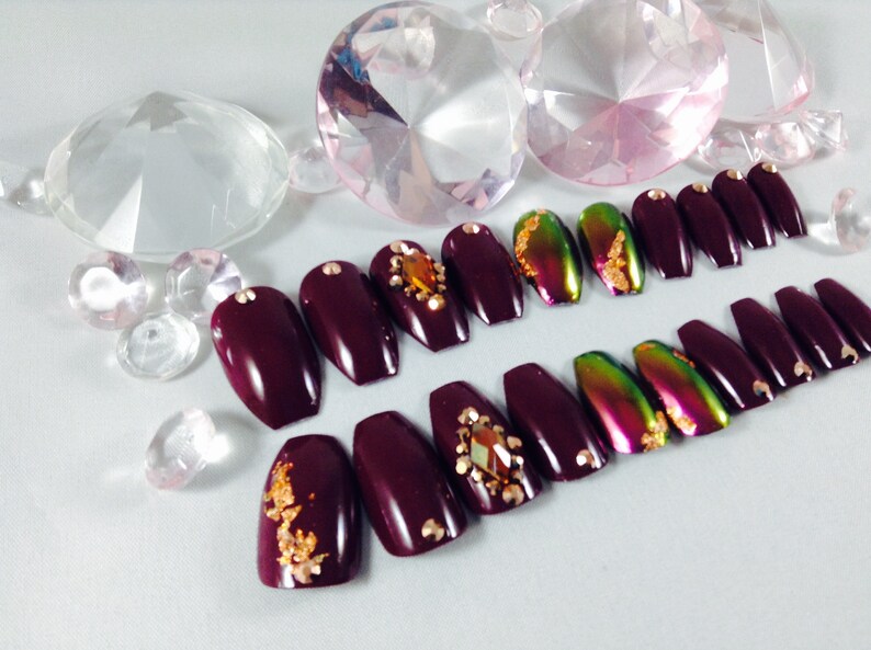 Puede incluir: U&ntilde;as postizas en forma de ata&uacute;d de color burdeos con detalles dorados y pedrer&iacute;a.