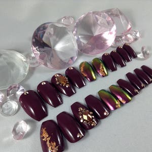 Puede incluir: U&ntilde;as postizas de ata&uacute;d color burdeos con detalles dorados y pedrer&iacute;a.