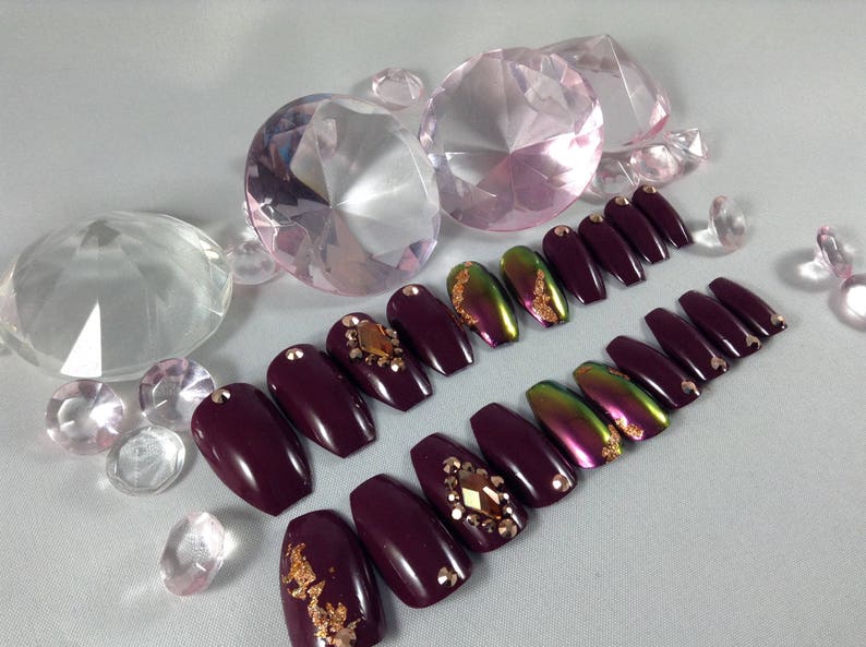 Puede incluir: U&ntilde;as postizas de ata&uacute;d color burdeos con detalles dorados y pedrer&iacute;a.