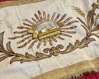 May include: Cream-colored textile with gold and brown embroidery. The design features a central sunburst with a sleeping figure, surrounded by wheat and floral patterns. A gold trim borders the edge.