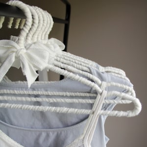 May include: White rope hangers with a light blue tank top and a white tank top with a floral pattern hanging on them.