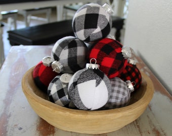 May include: A wooden bowl filled with plaid fabric Christmas ornaments in red, black, white, and gray.