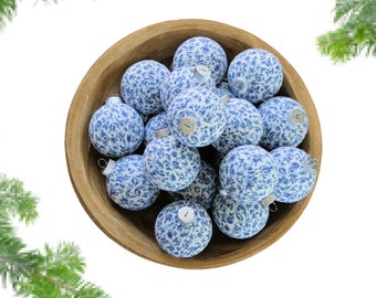 May include: A wooden bowl filled with blue and white patterned Christmas baubles. The baubles have a floral design and are arranged in a random pattern.