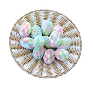 K&ouml;nnte beinhalten: Ein Weidenkorb gef&uuml;llt mit pastellfarbenen Karomuster-Ostereiern. Die Eier sind kreisf&ouml;rmig angeordnet und in den Farben Rosa, Blau und Gr&uuml;n gehalten.