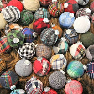 May include: A collection of handmade Christmas ornaments made from various plaid fabrics in red, green, blue, and white. The ornaments are all round and have a silver cap on top.