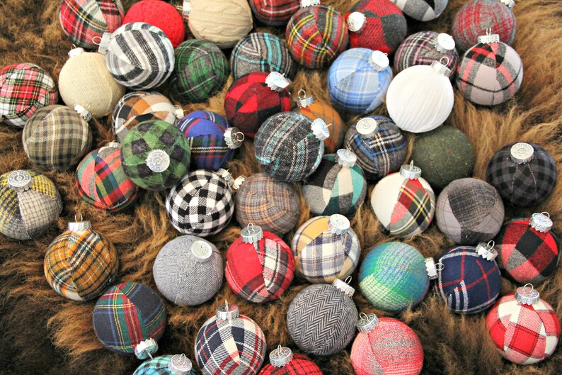 May include: A collection of handmade Christmas ornaments made from various plaid fabrics in red, green, blue, and white. The ornaments are all round and have a silver cap on top.
