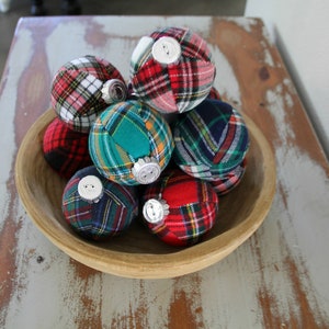 May include: A wooden bowl filled with plaid fabric Christmas ornaments. The ornaments are in various colors, including red, green, blue, and white.