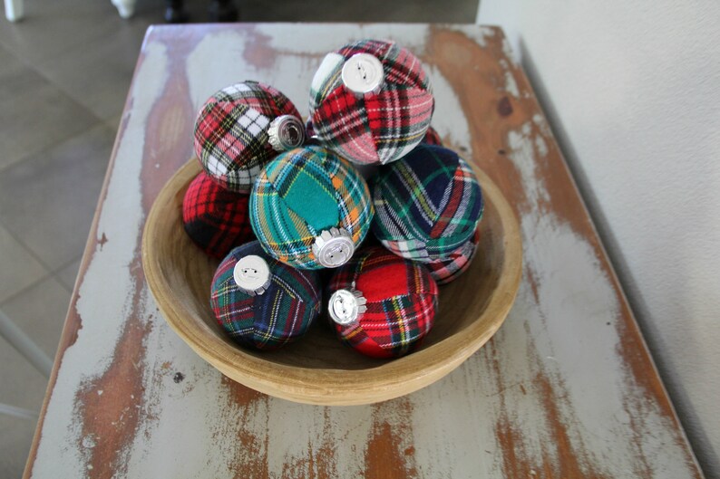 May include: A wooden bowl filled with plaid fabric Christmas ornaments. The ornaments are in various colors, including red, green, blue, and white.