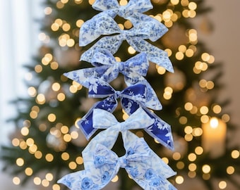 May include: A vertical stack of six fabric bows featuring various shades of blue and white floral patterns. Each bow has long, pointed tails and is constructed from patterned textile material, displaying a range of light to dark blue botanical prints.