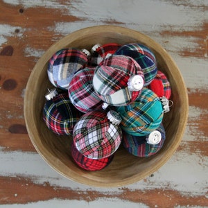 May include: A wooden bowl filled with plaid fabric Christmas ornaments. The ornaments are in various shades of red, green, blue, and white.