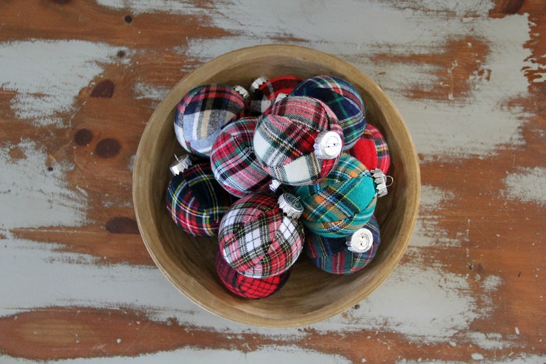 May include: A wooden bowl filled with plaid fabric Christmas ornaments. The ornaments are in various shades of red, green, blue, and white.