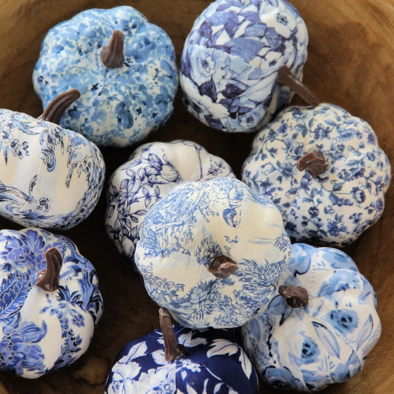 Pode incluir: Uma cole&ccedil;&atilde;o de nove ab&oacute;boras decorativas com v&aacute;rios padr&otilde;es florais, toile e bot&acirc;nicos em azul e branco. Cada ab&oacute;bora &eacute; rematada com um pequeno caule castanho. As ab&oacute;boras est&atilde;o dispostas juntas, exibindo uma mistura de estampados em azul claro e escuro sobre superf&iacute;cies de tecido branco, criando um conjunto coerente de artigos de decora&ccedil;&atilde;o sazonal estampados.