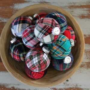 May include: A wooden bowl filled with plaid fabric Christmas ornaments. The ornaments are in various shades of red, blue, green, and white.