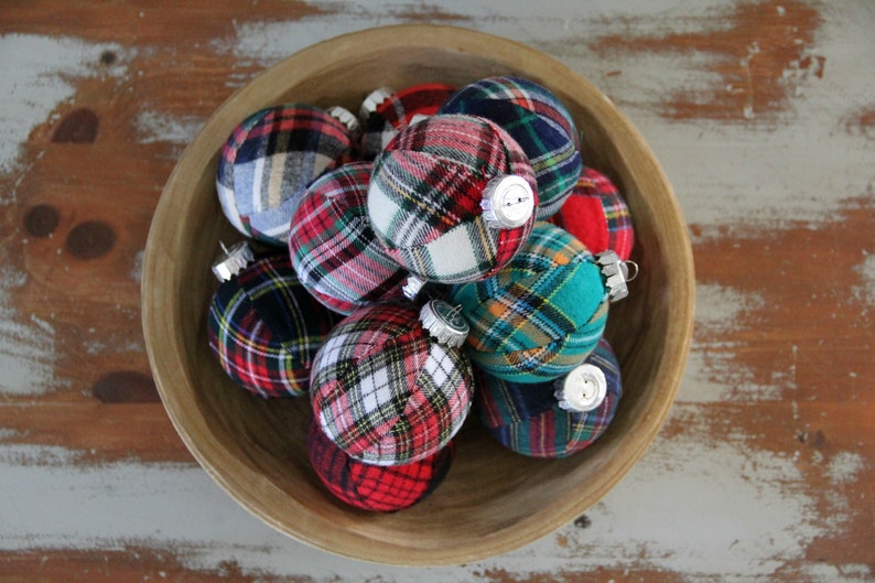 May include: A wooden bowl filled with plaid fabric Christmas ornaments. The ornaments are in various shades of red, blue, green, and white.