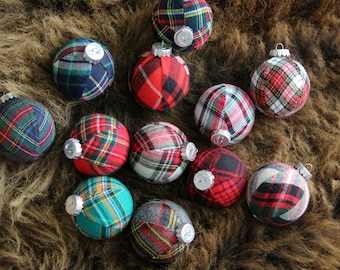 May include: A collection of 12 Christmas ornaments made from plaid fabric in various colors, including red, green, blue, and white. The ornaments are arranged on a brown furry surface.