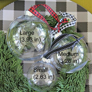 May include: Three clear glass Christmas ornaments of different sizes with black and white ribbon. The ornaments are labeled "Large (3.93 in)", "Medium (3.26 in)", and "Small (2.63 in)".