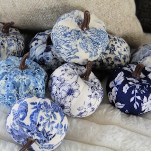 Pode incluir: Uma cole&ccedil;&atilde;o de ab&oacute;boras decorativas de tecido com v&aacute;rios padr&otilde;es florais, toile e bot&acirc;nicos em azul e branco. Cada ab&oacute;bora &eacute; rematada com um pequeno caule castanho e apresenta uma forma arredondada e segmentada com desenhos.