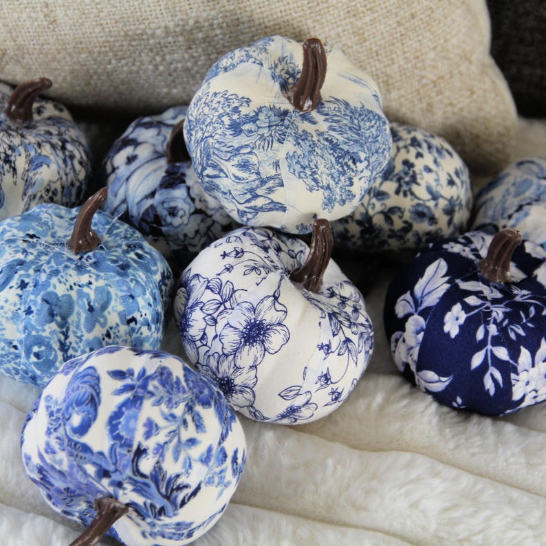 Pode incluir: Uma cole&ccedil;&atilde;o de ab&oacute;boras decorativas de tecido com v&aacute;rios padr&otilde;es florais, toile e bot&acirc;nicos em azul e branco. Cada ab&oacute;bora &eacute; rematada com um pequeno caule castanho e apresenta uma forma arredondada e segmentada com desenhos.