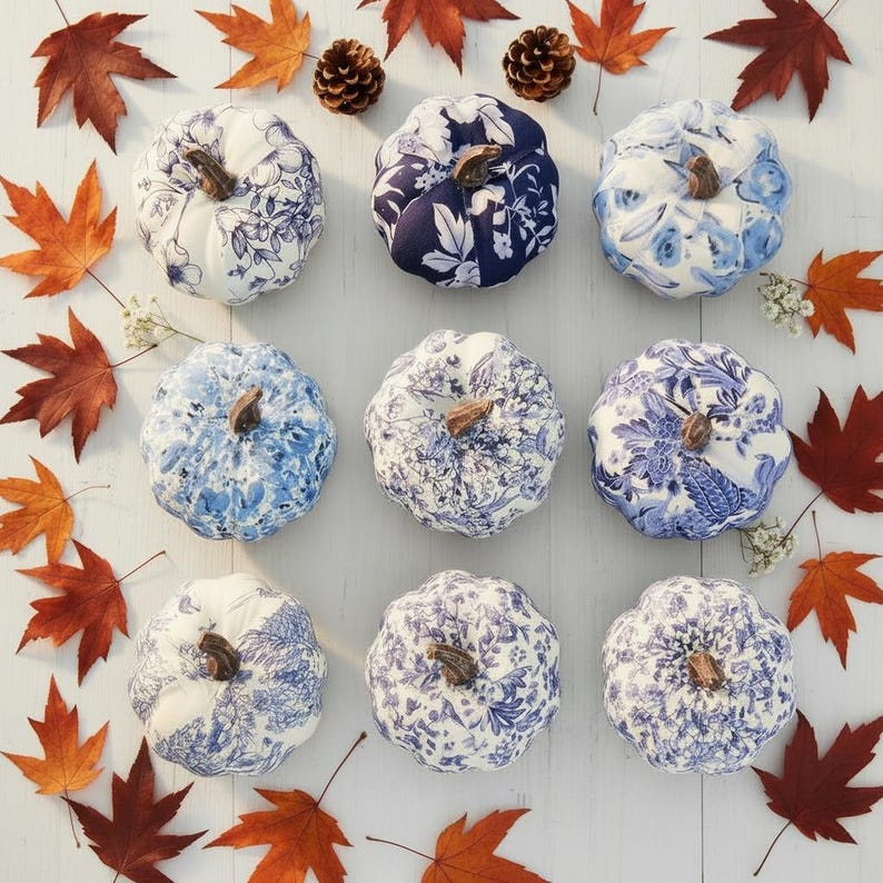 Pode incluir: Nove ab&oacute;boras de tecido dispostas numa grelha, cada uma com distintos padr&otilde;es florais ou toile em azul e branco. Cada ab&oacute;bora &eacute; rematada com um pequeno caule castanho. As ab&oacute;boras est&atilde;o rodeadas por folhas de &aacute;cer cor de laranja.