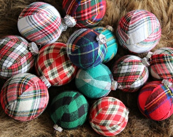 May include: A collection of round Christmas ornaments. Each ornament is covered in a plaid fabric in various colors, including red, green, blue, and white. The ornaments have silver-colored metal caps for hanging.