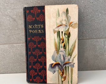 May include: Antique book titled "SCOTT'S POEMS." The spine is black with a red floral pattern. The cover features a watercolor illustration of irises in shades of white, blue, and yellow. The book is displayed on a white surface.