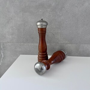 May include: A set of two wooden salt and pepper shakers with silver tops. The shakers are brown and have a textured finish.