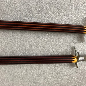 May include: Two steak knives with black and brown striped handles and yellow accents. The knives have a silver blade and a decorative handle.