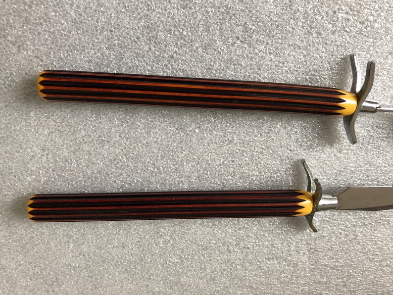 May include: Two steak knives with black and brown striped handles and yellow accents. The knives have a silver blade and a decorative handle.
