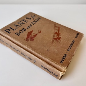 May include: A brown book titled "Planes for Bob and Andy" with illustrations of aeroplanes. The book is part of the "Core-Vocabulary Readers" series and is published by Macmillan. The authors are Huber, Salisbury, and Gates.