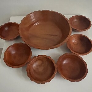 May include: Set of seven wooden bowls in various sizes. The bowls are all brown and have a natural wood finish. The largest bowl is a serving bowl with a scalloped edge.