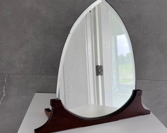 May include: A wooden framed oval mirror with a dark brown finish. The mirror is standing on a white surface.