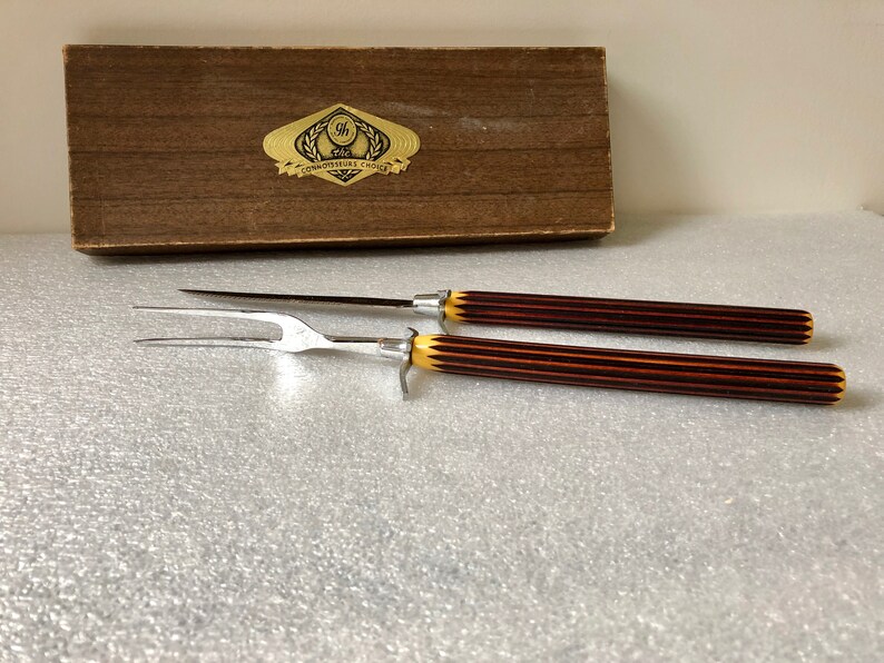 May include: A set of two carving tools with brown and yellow striped handles in a wooden box with the text "The Connoisseurs Choice" on the lid.