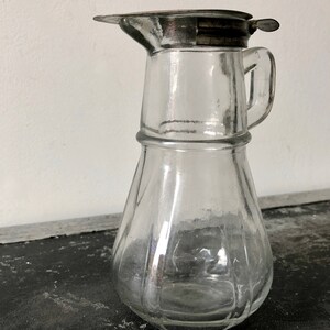 May include: A clear glass pitcher with a silver lid and a handle. The pitcher has a textured, ribbed design.