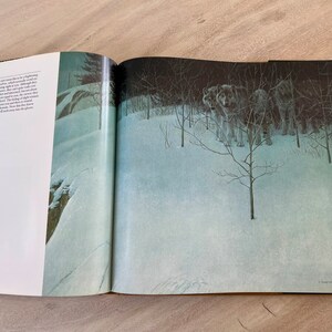 May include: A book open to a page with a painting of a snowy forest scene. The painting depicts a pack of wolves standing in the snow, with trees and bushes behind them. The text on the page reads "However, I do not see them as signifying menace. The shadows, which cast themselves over the snow, are not menacing. Although they are how and where they are, you never feel that they are on the attack. You never feel that they are a threat. They are doing what wolves do, and they are doing it in a way that is both beautiful and striking. Now the feeling of danger comes only from the viewer, and the viewer alone will make that decision."