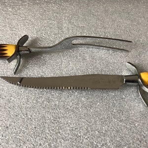 May include: A set of two kitchen utensils with black and yellow striped handles. The first utensil is a carving fork with two prongs. The second utensil is a serrated carving knife.