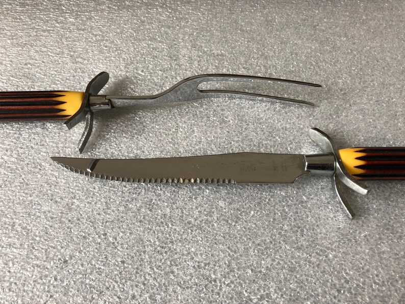 May include: A set of two kitchen utensils with black and yellow striped handles. The first utensil is a carving fork with two prongs. The second utensil is a serrated carving knife.