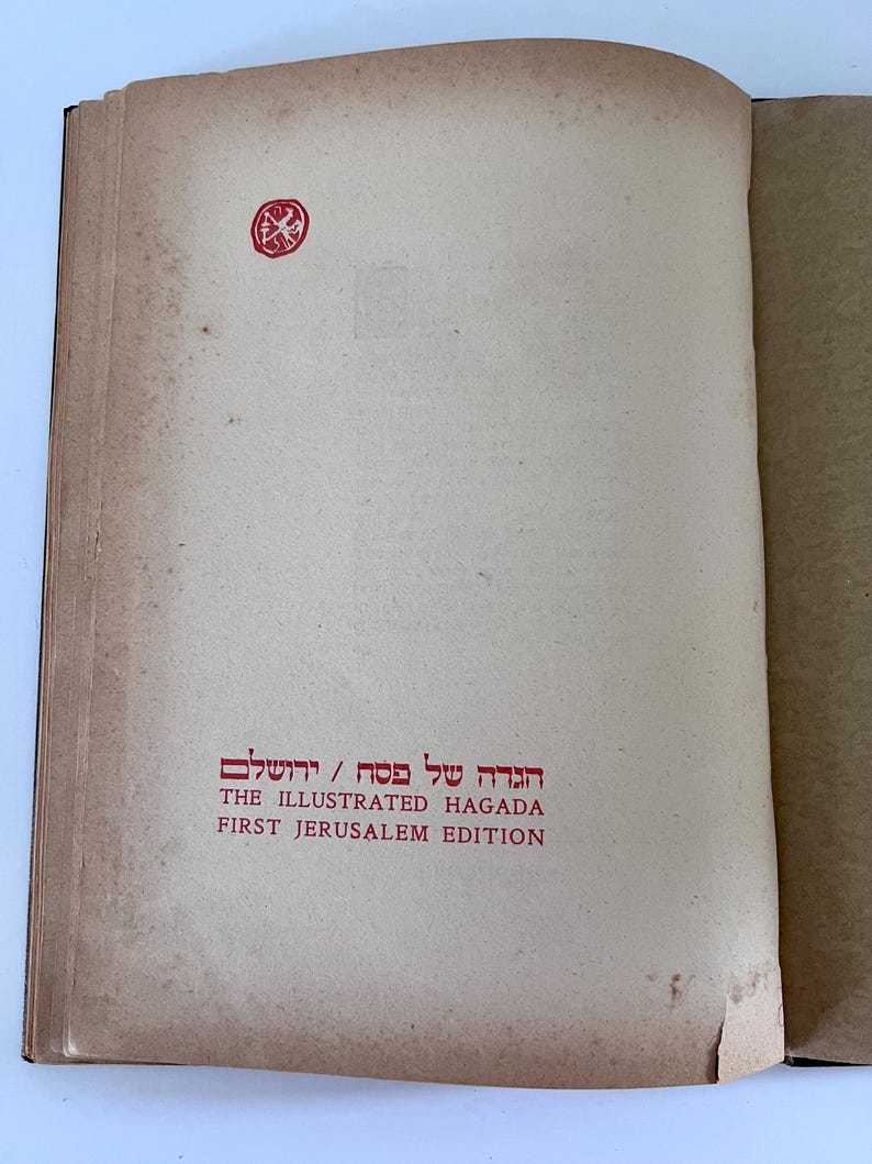 Puede incluir: Primer plano de la portada de un libro titulado "The Illustrated Haggadah, First Jerusalem Edition". La portada es de color marr&oacute;n claro con un sello rojo en la esquina superior izquierda.