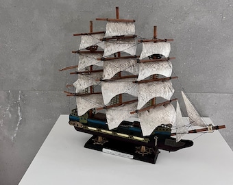 May include: A wooden model ship with white sails and a black hull. The ship is on a wooden base with a nameplate that reads "Constitution 1797".