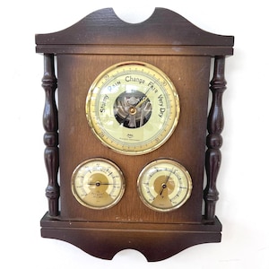 May include: A vintage wooden weather station with a barometer and two gauges. The barometer dial reads "Change Fair Very Dry" and "Stormy". The gauges display temperature and humidity readings. The frame is dark brown.