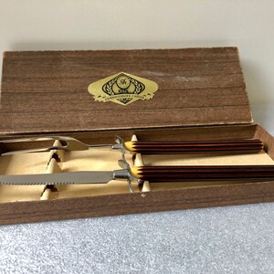 May include: A wooden box with a gold label that reads "The Connoisseur's Choice" and contains a carving knife and fork with brown and yellow handles.