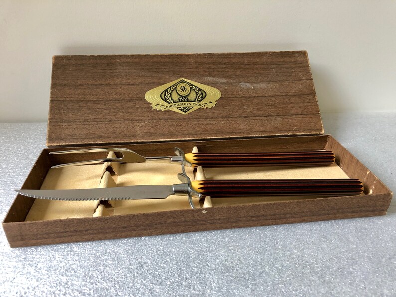 May include: A wooden box with a gold label that reads "The Connoisseur's Choice" and contains a carving knife and fork with brown and yellow handles.