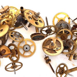 May include: A collection of vintage watch gears in various sizes and shapes, made of brass and other metals. The gears have a golden hue and show signs of age and wear, with some rust visible. The components are scattered, suggesting they are for repair or crafting.