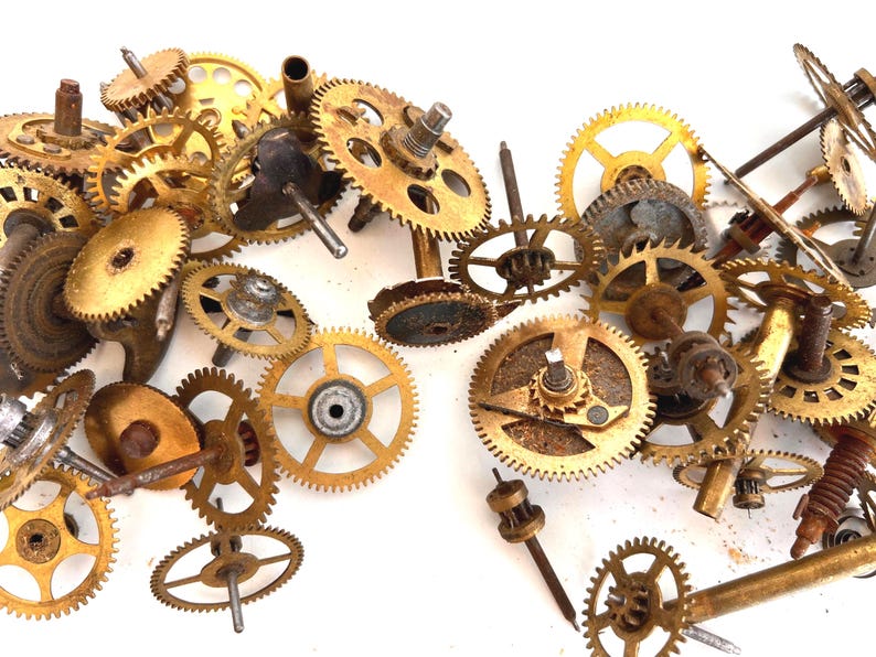 May include: A collection of vintage watch gears in various sizes and shapes, made of brass and other metals. The gears have a golden hue and show signs of age and wear, with some rust visible. The components are scattered, suggesting they are for repair or crafting.