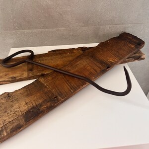 May include: A rusty metal hook with a curved handle, resting on two pieces of weathered wood.