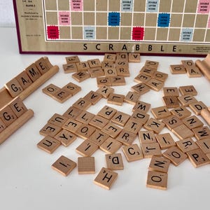 May include: A close-up of a Scrabble game in progress with wooden tiles spelling out words like "vintage", "game", "fun", and "scrabble".